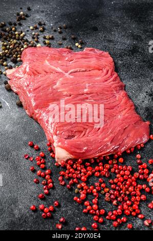 Rohes Flankensteak mit schwarzem und rosa Pfeffer. Schwarzer Hintergrund. Draufsicht Stockfoto