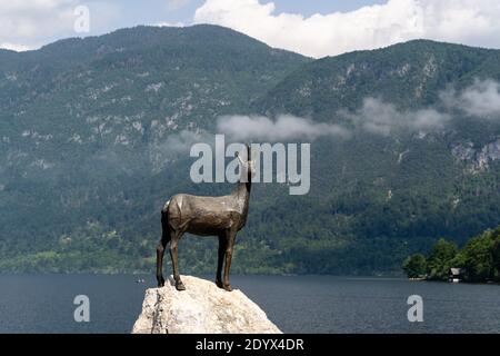 Schöne Aufnahme einer Statue auf Goldhorn im Bohinjer See Umgeben von Bergen und Bäumen Stockfoto