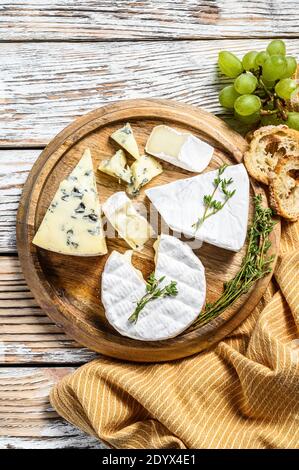Verschiedene Käsesorten auf einem runden Holzbrett. Camembert, Brie und Blauschimmelkäse mit Trauben. Weißer Holzhintergrund. Draufsicht Stockfoto