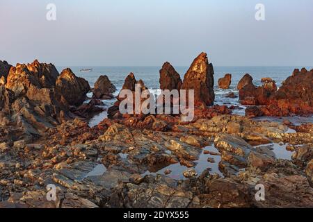 Morgendliches Seascape. Schöne Klippen in Ufernähe und ein Fischerboot. Fischer fangen am frühen Morgen Fisch. Arambol, Goa, Indien Stockfoto