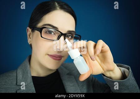 Junge Frau in einer Brille, die die Kamera anschaut und Nasenspray vor sich hält. Stockfoto