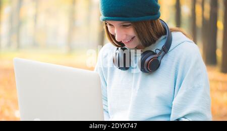 Glückliches Mädchen mit Kopfhörern und Laptop im herbstlichen Park Stockfoto