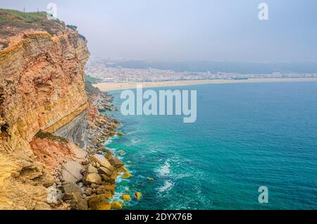 Luftaufnahme von Felsen und Klippen, azurblauem türkisfarbenem Wasser des Atlantischen Ozeans und Sandstrand Küste Praia da Nazare Stadt, Leiria District, Oeste Region Stockfoto