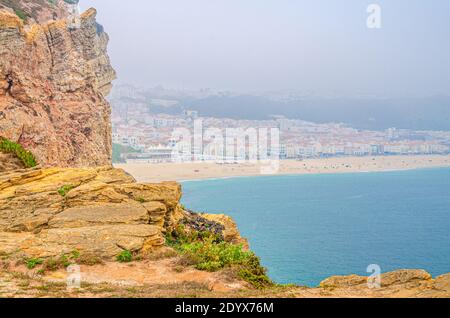 Blick von oben auf Felsen und Klippen, azurblaues türkisfarbenes Wasser des Atlantischen Ozeans und Sandstrand Küste Praia da Nazare Stadthintergrund, Leiria District, Oest Stockfoto