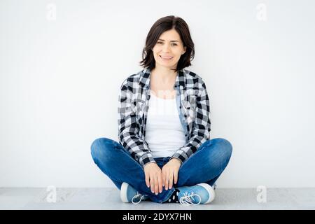 Lächelnde Frau sitzt auf dem Boden auf weißem Wandhintergrund Stockfoto