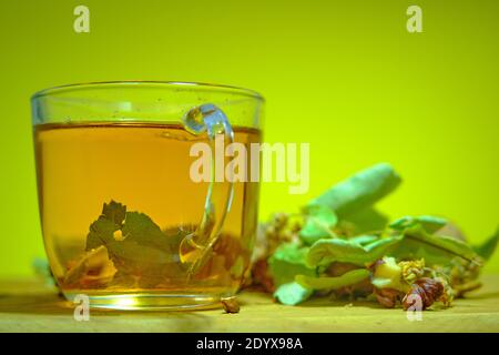 Foto von Kräuter- und Lindentee in der Glaskanne zusammen mit Lindenteeblättern und gebrochenen und nicht gebrochenen Walnüssen auf dem Holztisch. Stockfoto