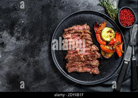 Geschnittenes, gegrilltes Rindfleisch marmoriertes, seltenes Steak. Chuck Augenrolle auf einem Teller mit einer Beilage von Gemüse. Schwarzer Hintergrund. Draufsicht. Speicherplatz kopieren Stockfoto