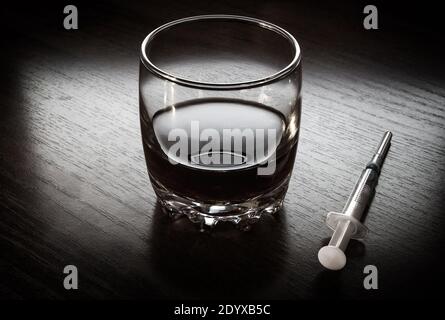 Ein Glas Whiskey und eine Spritze auf dem Tisch Im dunklen Raum Stockfoto
