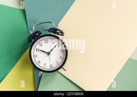 Schwarzer Wecker auf geometrischem grünem Papierhintergrund. Minimaler Stil Kopierbereich Ansicht von oben Vorlage für Ihren Text, Design. Stockfoto