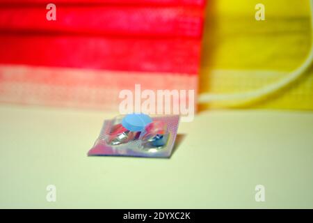 Blaue Pillen auf der metallischen Farbe seiner Verpackung und bunten medizinischen Masken Hintergrund. Stockfoto