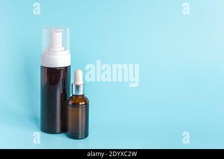 Kleine braune Tropfflasche und große Flasche mit weißem Spender auf blauem Hintergrund. Konzept Beauty Kosmetik Produkt. Stockfoto