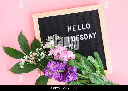 Hallo Dienstag Text auf schwarzem Briefbrett und Blumenstrauß bunte Blumen auf rosa Hintergrund. Konzept Happy Tuesday. Vorlage für Postkarte, Grußkarte Stockfoto