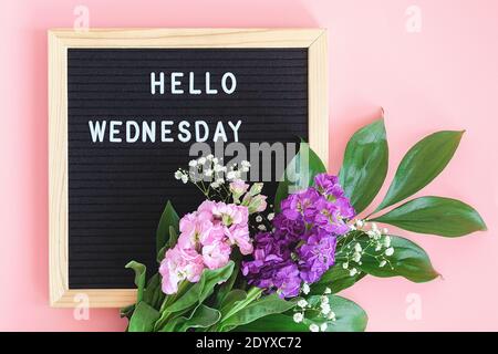 Hallo Mittwoch Text auf schwarzem Briefbrett und Blumenstrauß bunte Blumen auf rosa Hintergrund. Konzept Happy Wednesday. Vorlage für Postkarte, Gruß c Stockfoto