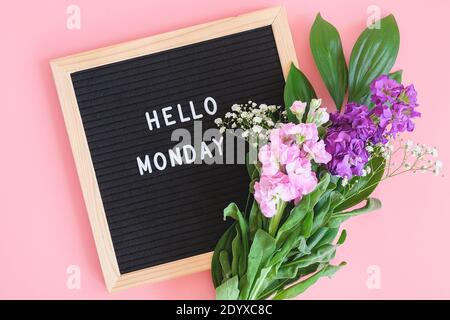 Hallo Montag Text auf schwarzem Briefbrett und Blumenstrauß bunte Blumen auf rosa Hintergrund. Konzept Happy Monday. Vorlage für Postkarte, Grußkarte FL Stockfoto