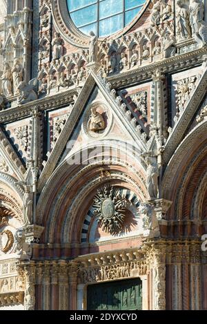 Prächtig verzierte Fassade mit Ornamenten und Skulpturen auf dem Hauptportal der Kathedrale von Siena im Sonnenlicht, Toskana, Italien Stockfoto