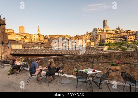 Junge Paare essen auf der Terrasse eines Restaurants mit Blick auf die mittelalterliche Altstadt von Siena in der Abendsonne, Toskana, Italien Stockfoto