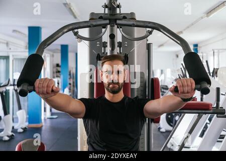 Mann trainiert auf einem Gerät in der Turnhalle. Konzentrieren Sie sich auf ihn. Stockfoto