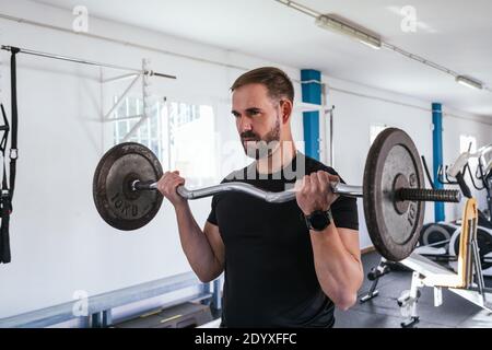 Junger Mann tut Bizeps Curl mit Bar. Bar Übung. Konzept von Gesundheit und Wohlbefinden Stockfoto