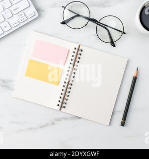 Draufsicht auf Bürotisch Schreibtisch gemütliches Arbeitskonzept mit Tastatur, Notizbuch, Bleistift, Brille und Kaffee auf hellem Marmor weißem Hintergrund. Stockfoto