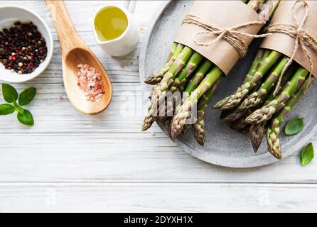 Bündel von rohen Spargelstämmen mit verschiedenen Gewürzen und Zutaten auf Holzhintergrund. Draufsicht, flach liegend. Stockfoto