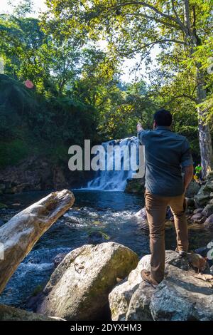 Ein junger Mann, der auf einem Felsen steht und auf einen Wasserfall in Xico, Veracruz, Mexiko zeigt Stockfoto