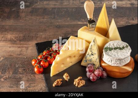 Sammlung von Schweizer, französischen, italienischen und holländischen Käsesorten auf einer schwarzen Käseplatte serviert mit Obst, Nüsse auf einer schwarzen Schiefertafel. Holztisch. Draufsicht Stockfoto