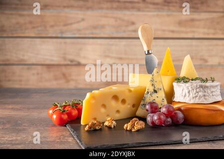 Verschiedene Käsesorten auf rustikalem Holztisch. Käseplatte: Parmesan, Cheddar, gouda, Camembert, Brie mit Nüssen auf Holzbrett auf dunklem Hintergrund w Stockfoto