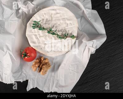 Köstlicher Brie-Käse, Walnüsse und Tomate auf Papier auf schieferschwarzem Hintergrund. Brie Art von Käse. Camembert. Frischer Brie-Käse und eine Scheibe auf Stein b Stockfoto