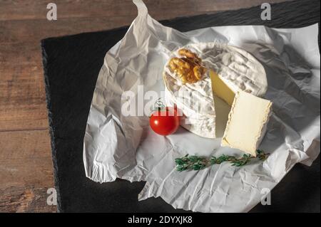 Köstlicher Brie-Käse, Walnüsse und Tomate auf Papier auf schieferschwarzem Hintergrund. Brie Art von Käse. Camembert. Frischer Brie-Käse und eine Scheibe auf Stein b Stockfoto