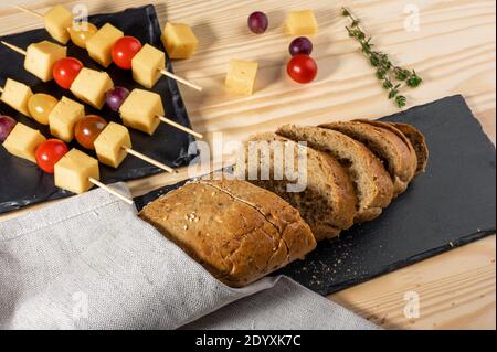 Fingerfood. Scheiben Käse und Tomaten auf einem Spieß. Italienische Vorspeise Spieße mit Käse, Kirschtomaten und Oliven auf Holzstäbchen auf einem schwarzen Stockfoto
