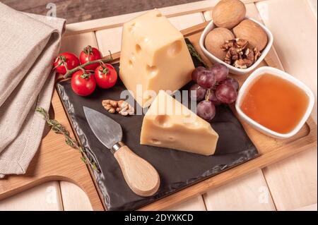 Käse maasdam mit Nüssen, Honig, Trauben und Tomaten auf Holzbrett und Tablett. Käse Dessert. Getöntes Bild Stockfoto