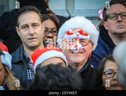 Mann in Weihnachtsmütze und Comedy-Weihnachtsbrille, lächelt in Zuschauermenge, London, England, Großbritannien Stockfoto