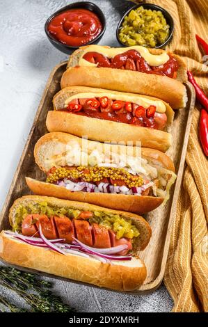 Hot Dogs voll beladen mit verschiedenen Belägen auf einem Tablett. Leckere Hot Dogs mit Schwein- und Rinderwürsten. Weißer Hintergrund. Draufsicht Stockfoto