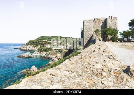 Blick von der Burgmauer des Schlosses Rocca Aldobrandesca in Talamone auf die Felsküste mit dem Lido Bagno delle Donne im Sommer, Toskana, Italien Stockfoto