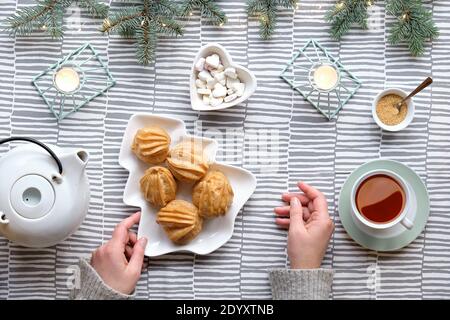 Kreative Tischaufstellung für Weihnachtstee. Kreative flache Lay mit Eclirs oder Braukuchen. Weihnachtsbaum Form Teller mit Kuchen, weibliche Hände. Stripy Stockfoto