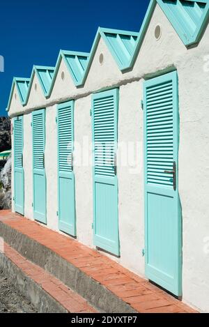 Umkleidekabinen mit türkisfarbenen Türen an einer weißen Fassade in strahlendem Sonnenschein im mundanen Bagno delle Donne Badebereich in Talamone, Toskana, Italien Stockfoto