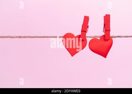 Zwei rote Herzen sind auf Clips mit Platz für Text auf einem rosa Hintergrund aufgehängt. Valentinstag Feiertage und Jubiläum Konzept. Stockfoto