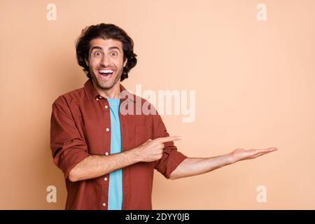 Portrait von attraktiven erstaunt fröhlichen Kerl hält auf Palm Kopie Raum Werbelösung isoliert über beige Pastellfarben Hintergrund Stockfoto
