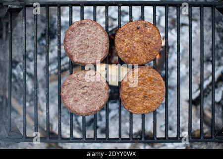 Fleischrindburger (L) und vegane Burger auf Pflanzenbasis (R) Kochen Sie Seite an Seite auf einem offenen Feuer Stockfoto