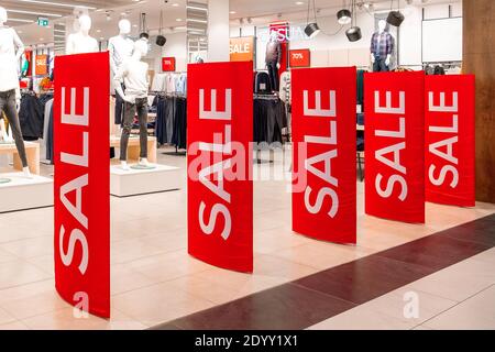 Große rote Tafeln mit einem Verkaufsschild am Eingang zu einem Bekleidungsgeschäft. Auf dem Hintergrund sind Dummy und Kleiderbügel. Promotion, Werbung, Shopping und b Stockfoto