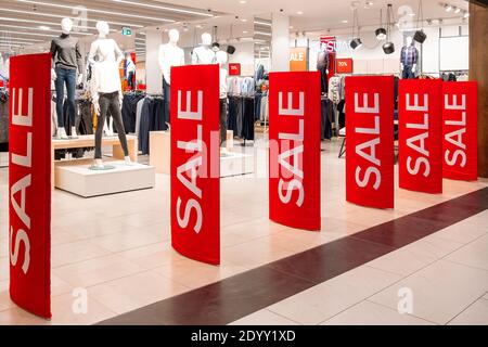Rote Werbetafeln stehen am Eingang einer Bekleidungsboutique mit Verkaufsinformationen. Im Hintergrund sind Übungspuppen und Kleiderbügel. Werbung, Werbung, Stockfoto