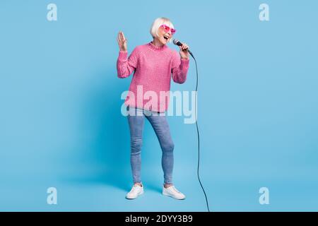 Foto-Portrait Ganzkörperansicht der alten Dame singen halten Mikrofon in einer Hand isoliert auf pastellblauem Hintergrund Stockfoto