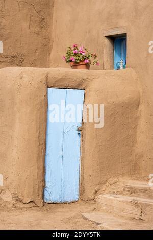 Nahaufnahme eines lehmziegelhauses mit blau bemalter Tür und einem Topf Geranien. Das historische indianische adobe Dorf Taos Pueblo, New Mexi Stockfoto