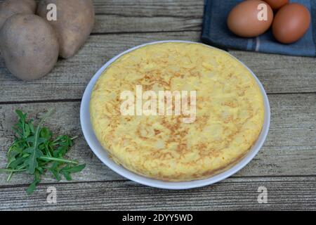 Spanische Omelette oder Tortilla de Patatas auf einem Teller mit frischen Eiern und Kartoffeln auf rustikalem Holzhintergrund. Stockfoto