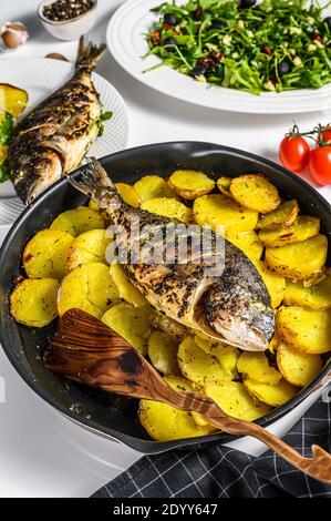 Abendessen mit gegrilltem Fisch aus der Meeresbrasse, Rucola-Salat mit Tomaten, gebackene Kartoffeln. Weißer Hintergrund. Draufsicht Stockfoto