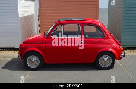 Classic Red Fiat 500 Motorwagen an der Strandpromenade vor Strandhütten geparkt. Stockfoto