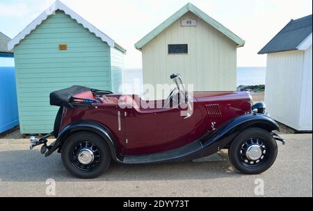 Classic Red Motor Car auf der Strandpromenade geparkt vor Strandhütten. Stockfoto