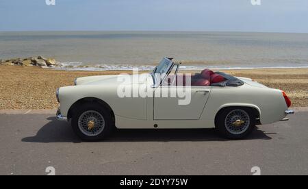 Classic White - Creme MG Midget Auto an der Strandpromenade mit Meer im Hintergrund geparkt. Stockfoto