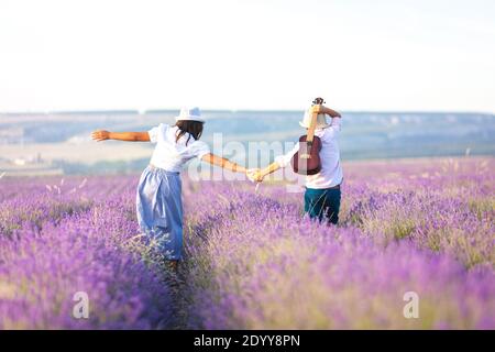Mädchen und Jungen mit einer Gitarre in den Händen in Lavendelfeld. Der Blick von hinten. Stockfoto