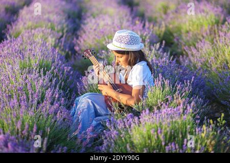 Schöne Landmädchen mit einer kleinen Gitarre in den Händen Ruhe in einem Lavendelfeld Stockfoto